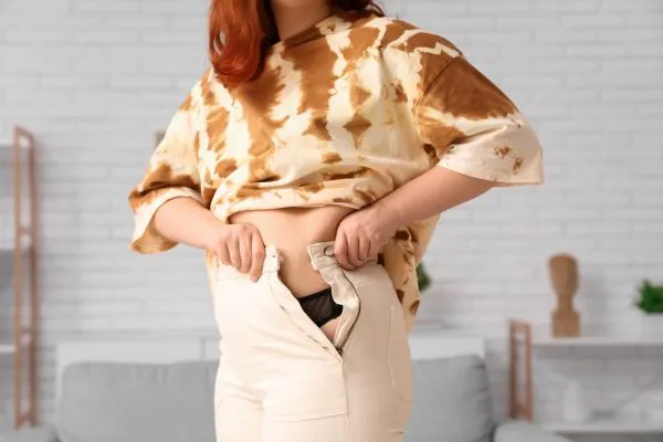 Image of woman trying to do her trousers up after pregnancy weight gain Waverley